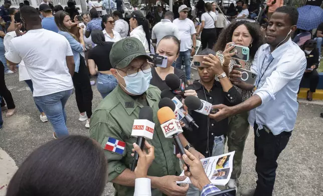 Colonel Valdez speaks to reporters at the National Institute of Forensic Pathology in Santo Domingo, Dominican Republic, Wednesday, April 9, 2025, while holding photos of people who remain missing after a roof collapsed at the Jet Set nightclub during a merengue concert. (AP Photo/Marvin Del Cid)