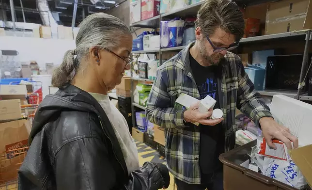 Pantry director Christopher Lowrance looks for items requested by Beth Anne Mollett, left, at the Bishop Sullivan Center food pantry, Tuesday, April 15, 2025, in Kansas City, Mo. (AP Photo/Charlie Riedel)