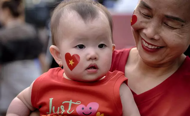 A baby girl sporting a heart with a yellow star takes in the festivities for the national celebrations of the 50th Anniversary of reunification and the end of the Vietnamese War, in Ho Chi Minh City, Vietnam, on Tuesday, April 29, 2025. (AP Photo/Richard Vogel)