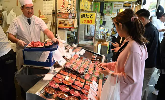 Customers look to buy tuna sushi meals at a market in Tokyo, Japan, Thursday, April 10, 2025. (AP Photo/Ayaka McGill)