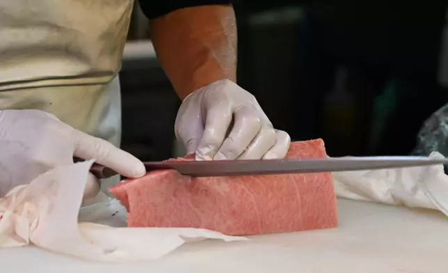 A knife cuts into a fatty cut of tuna at a market in Tokyo Thursday, April 10, 2025. (AP Photo/Ayaka McGill)