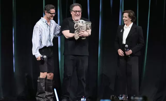 Actor Pedro Pascal, left, and Sigourney Weaver, right, with director Jon Favreau interact with "Grogu," a movie character, during a fan convention called the Star Wars Celebration Japan in Chiba, near Tokyo, Friday, April 18, 2025. (AP Photo/Hiro Komae)