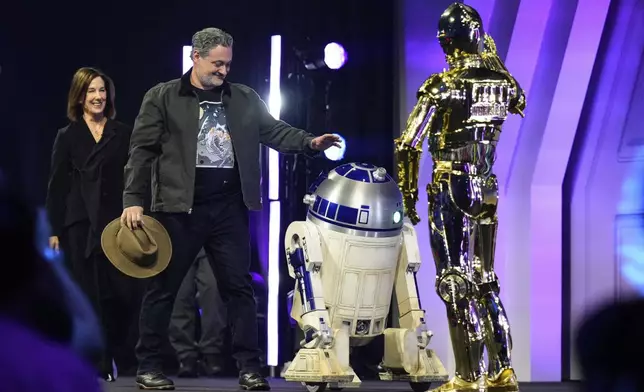 Film producer Kathleen Kennedy, left, and director Dave Filoni are welcomed by R2-D2 and C-3PO, right, as they appear on stage during a fan convention called the Star Wars Celebration in Chiba, near Tokyo, Friday, April 18, 2025. (AP Photo/Hiro Komae)