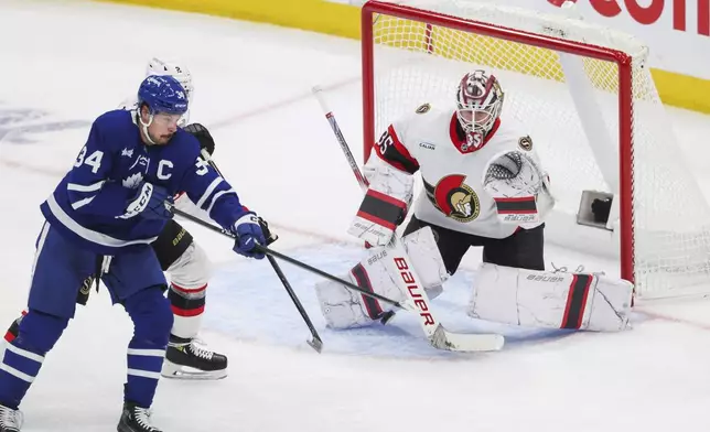 Toronto Maple Leafs' Auston Matthews (34) tips a puck toward Ottawa Senators goaltender Linus Ullmark (35) while being defended by Ottawa Senators' Artem Zub (2) during second period NHL playoff action in Toronto on Tuesday, April 22, 2025. (Cole Burston/The Canadian Press via AP)