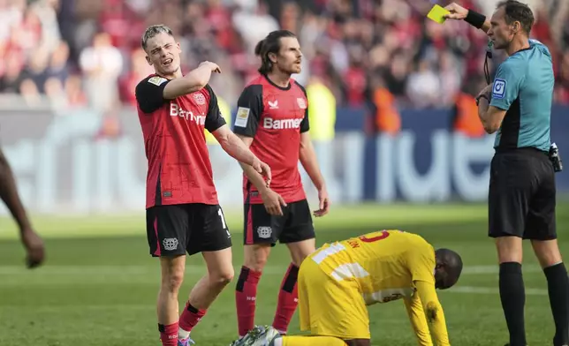 Referee Bastian Dankert shows a yellow card to Leverkusen's Florian Wirtz, left, during the German Bundesliga soccer match between Bayer Leverkusen and Union Berlin at the BayArena in Leverkusen, Germany, Saturday, April 12, 2025. (AP Photo/Martin Meissner)