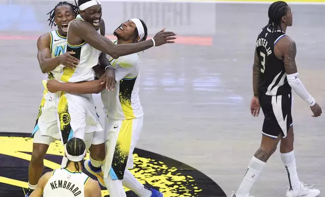 Indiana Pacers teammates Aaron Nesmith, left, Pascal Siakam, center, and Myles Turner, right, celebrate the team's win after overtime in Game 5 of an NBA basketball first-round playoff series as Milwaukee Bucks guard Kevin Porter Jr. (3) walks off the court in Indianapolis, Tuesday, April 29, 2025. (AP Photo/Michael Conroy)