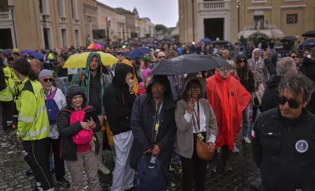 People wait in line under the rain to enter St. Peter's Basilica to view Pope Francis lying in state, at the Vatican, Thursday, April 24, 2025. (AP Photo/Francisco Seco)