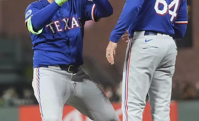 Texas Rangers' Joc Pederson, left, gestures next to first base coach Corey Ragsdale (64) after an RBI single against the San Francisco Giants during the sixth inning of a baseball game in San Francisco, Friday, April 25, 2025. (AP Photo/Jeff Chiu)