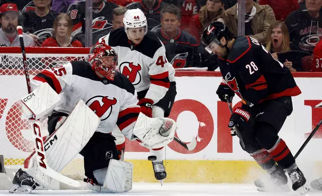 Carolina Hurricanes' William Carrier (28) tries to gain control of the puck in front of New Jersey Devils goaltender Jacob Markstrom (25) and Dennis Cholowski (44) during the third period of Game 2 of an NHL hockey Stanley Cup first-round playoff series in Raleigh, N.C., Tuesday, April 22, 2025. (AP Photo/Karl DeBlaker)
