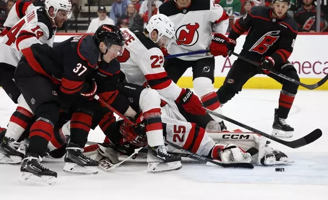 New Jersey Devils' Brett Pesce (22) reaches for the puck to save a potential goal with Carolina Hurricanes' Andrei Svechnikov (37) nearby during the second period of Game 2 of an NHL hockey Stanley Cup first-round playoff series in Raleigh, N.C., Tuesday, April 22, 2025. (AP Photo/Karl DeBlaker)
