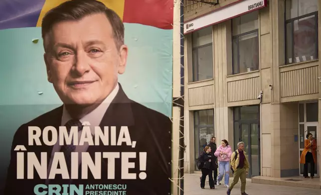 People walk by a poster of Crin Antonescu, the presidential candidate backed by Romania's governing coalition candidate in the upcoming May elections in Bucharest, Romania, Friday, March 28, 2025. (AP Photo/Vadim Ghirda)