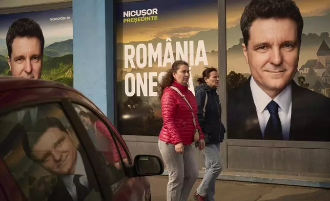 Women walk by posters of Nicusor Dan, the mayor of Bucharest and presidential candidate in the upcoming May elections in Bucharest, Romania, Friday, March 28, 2025. (AP Photo/Vadim Ghirda)