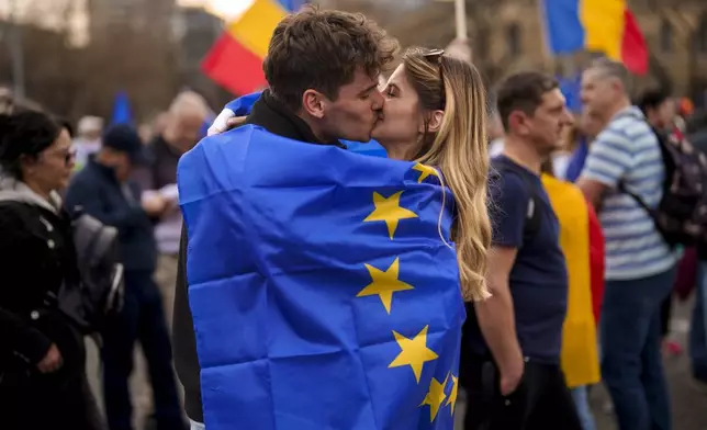 Young people kiss, wrapped in the European Union flag, at a pro-European rally, joined by thousands, to counter what the organizers described as a "wave of sovereignism and ultranationalism" in Bucharest, Romania, Saturday, March 15, 2025. (AP Photo/Vadim Ghirda)