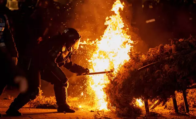 FILE- A riot policeman attempts to extinguish a fire as supporters of Calin Georgescu protested the electoral body's decision to reject his candidacy in a presidential election redo in Bucharest, Romania, Sunday, March 9, 2025. (AP Photo/Vadim Ghirda, File)