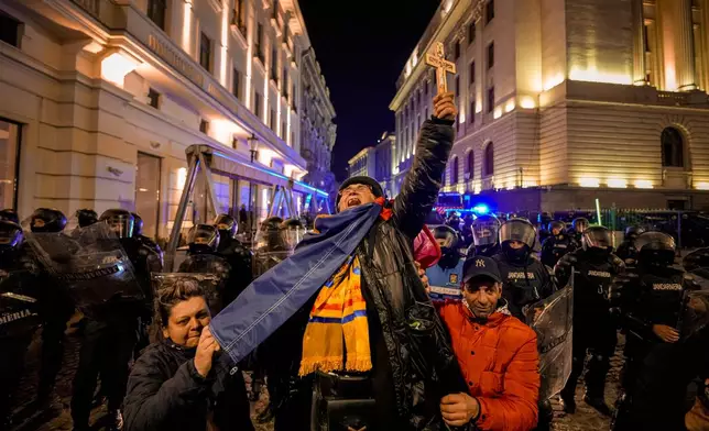 FILE - A woman screams holding a cross in front of riot policemen blocking a street following clashes with supporters of Calin Georgescu after Romania's electoral body rejected his candidacy in the presidential election rerun in Bucharest, Romania, Monday, March 10, 2025. (AP Photo/Andreea Alexandru, File)