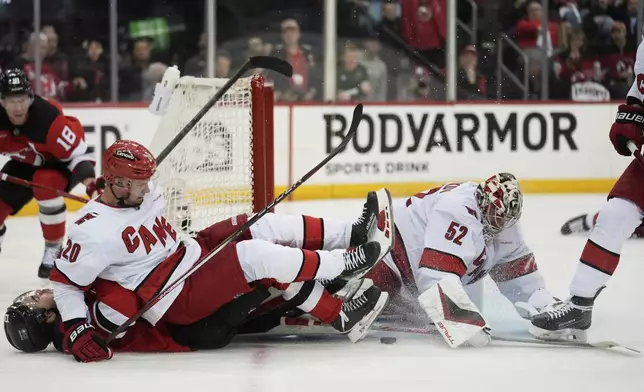 Carolina Hurricanes goaltender Pyotr Kochetkov, right, makes a save as Sebastian Aho, top left, hits New Jersey Devils' Nico Hischier, bottom left, during the second period of Game 4 of an NHL hockey first-round series, Sunday, April 27, 2025, in Newark, N.J. (AP Photo/Seth Wenig)