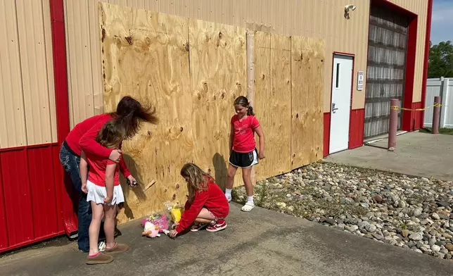 Jennifer Walston, 43, hugs daughter Lexi Walston, 6, while sisters Briley Walston, 9 and Madison Foster, 10, place flowers and stuffed animals at the site where several were killed Monday, when a car barreled through a building used for an after-school camp in Chatham, Ill., on Tuesday, April 29, 2025. (AP Photo/John O'Connor)