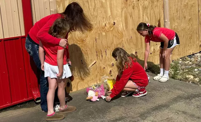 Jennifer Walston, 43, hugs daughter Lexi Walston, 6, while sisters Briley Walston, 9 and Madison Foster, 10, place flowers and stuffed animals at the site where several were killed Monday, when a car barreled through a building used for an after-school camp in Chatham, Ill., on Tuesday, April 29, 2025. (AP Photo/John O'Connor)