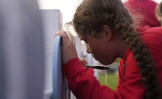 Nine-year-old Coralie Glessner writes on a heart for Alma Buhnerkempe at a vigil for three young children and a teenager, including Buhnerkempe, who were killed when a car barreled through a building used for an after-school camp Tuesday, April 29, 2025, in Chatham, Ill. (AP Photo/Erin Hooley)