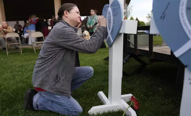 Sue Meyer writes on a heart for Rylee Britton at a vigil for three young children and a teenager, including Britton, who were killed when a car barreled through a building used for an after-school camp Tuesday, April 29, 2025, in Chatham, Ill. (AP Photo/Erin Hooley)