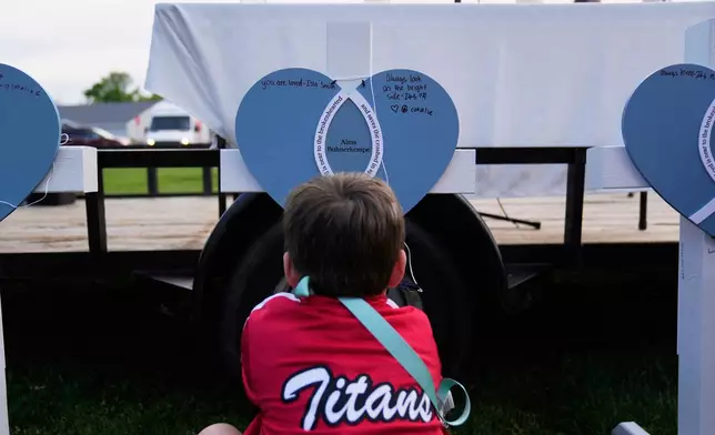 Seven-year-old Harriet Glessner writes on a heart for Alma Buhnerkempe at a vigil for three young children and a teenager, including Buhnerkempe, who were killed when a car barreled through a building used for an after-school camp Tuesday, April 29, 2025, in Chatham, Ill. (AP Photo/Erin Hooley)
