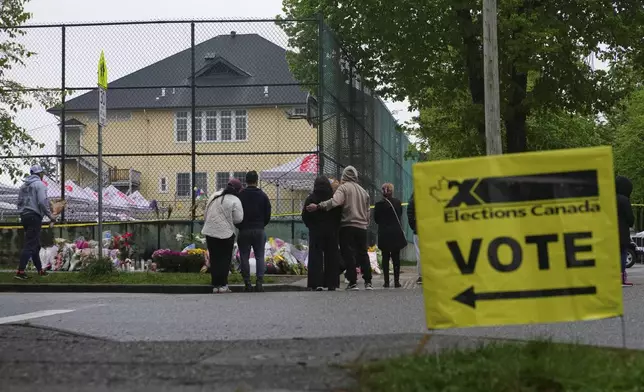 A voting sign stands near a memorial for victims after a vehicle drove into a crowd during a Filipino heritage festival in Vancouver, British Columbia, Monday, April 28, 2025. (AP Photo/Lindsey Wasson)