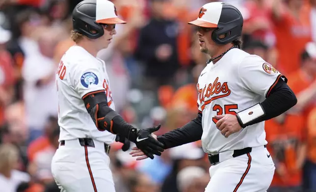 Baltimore Orioles' Adley Rutschman (35) celebrates with designated hitter Heston Kjerstad, left, after scoring on an RBI hit in by Ryan Mountcastle during the first inning of an opening-day baseball game against the Boston Red Sox, Monday, March 31, 2025, in Baltimore. (AP Photo/Stephanie Scarbrough)