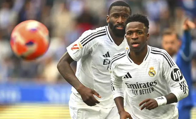 Real Madrid's Vinicius Junior, right and Antonio Rudiger chase the ball during a Spanish La Liga soccer match between Alaves and Real Madrid at the Mendizorroza stadium in Vitoria, Spain, Sunday April 13, 2025. (AP Photo/Miguel Oses)