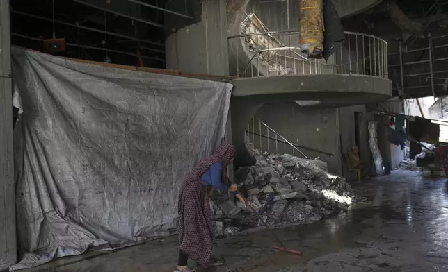 Karima Al-Kafarna cleans the hallway outside her family's makeshift home inside the destroyed Rashad Al-Shawa Cultural Center in Gaza City, Monday, April 21, 2025. (AP Photo/Jehad Alshrafi)