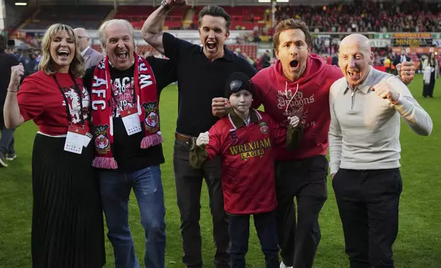 Wrexham co-owners Rob McElhenney, center, and Ryan Reynolds, second right, celebrate at the end of the English League One soccer match between Wrexham and Charlton Athletic at the Racecourse ground in Wrexham, Wales, Saturday, April 26, 2025. (AP Photo/Jon Super)