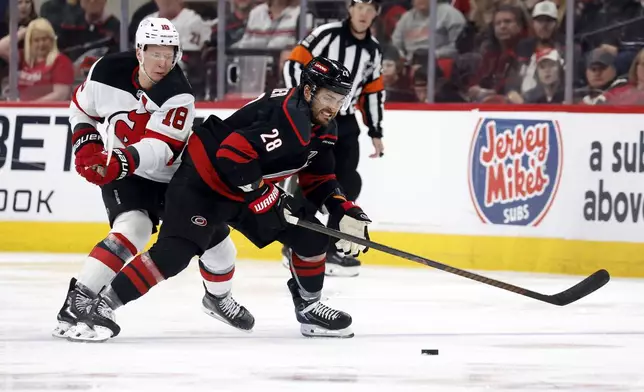 Carolina Hurricanes' William Carrier (28) tries to move the puck away from New Jersey Devils' Ondrej Palat (18) during the first overtime period of Game 5 of an NHL hockey Stanley Cup first-round playoff series in Raleigh, N.C., Tuesday, April 29, 2025. (AP Photo/Karl DeBlaker)