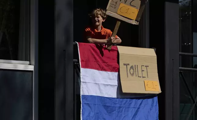 A boy earns some money by charging one euro for the use of a private's home bathroom as people celebrate King's Day in Amsterdam, Netherlands, Saturday, April 26, 2025. (AP Photo/Peter Dejong)