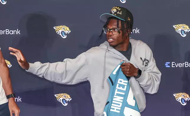 Two-way player Travis Hunter, the Jacksonville Jaguars first round draft pick, second overall, strikes a Heisman pose while holding a jersey during an NFL football press conference, Friday, April 25, 2025, in Jacksonville, Fla. (AP Photo/Gary McCullough)