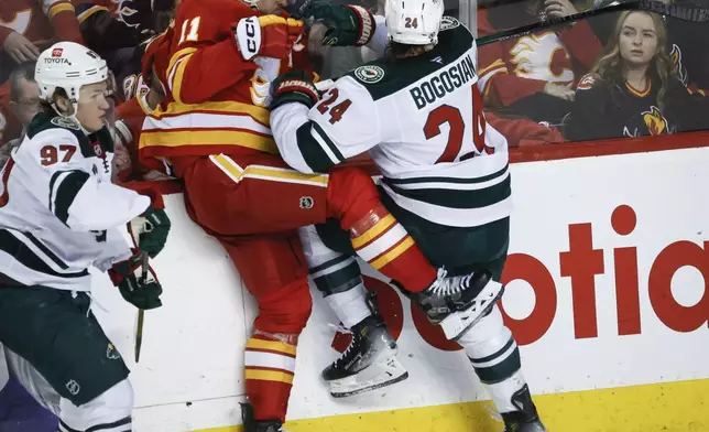 Minnesota Wild's Zach Bogosian (24) checks Calgary Flames' Mikael Backlund (11) during the second period of an NHL hockey game in Calgary, Alberta, Friday, April 11, 2025. (Jeff McIntosh/The Canadian Press via AP)
