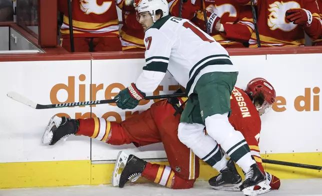 Minnesota Wild's Marcus Foligno (17) checks Calgary Flames' Rasmus Andersson (4) during the first period of an NHL hockey game in Calgary, Alberta, Friday, April 11, 2025. (Jeff McIntosh/The Canadian Press via AP)