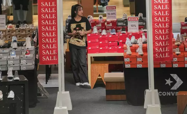 A shop clerk waits for customers behind a sales advertisement at a shopping mall in Bangkok, Thailand, Wednesday, April 9, 2025. (AP Photo/Sakchai Lalit)