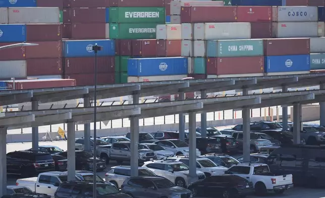 Vehicles are parked under solar panels as shipping containers sit stacked at the Long Beach Container Terminal in Long Beach, Calif., on Tuesday, April 8, 2025. (AP Photo/Damian Dovarganes)
