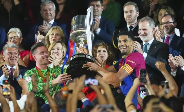 Barcelona's Ronald Araujo, center right, and Barcelona's goalkeeper Marc-Andre ter Stegen lift the trophy after winning the Spanish Copa del Rey final soccer match between Barcelona and Real Madrid at Estadio de La Cartuja stadium in Seville, Spain, Sunday, April 27, 2025. (AP Photo/Jose Breton)