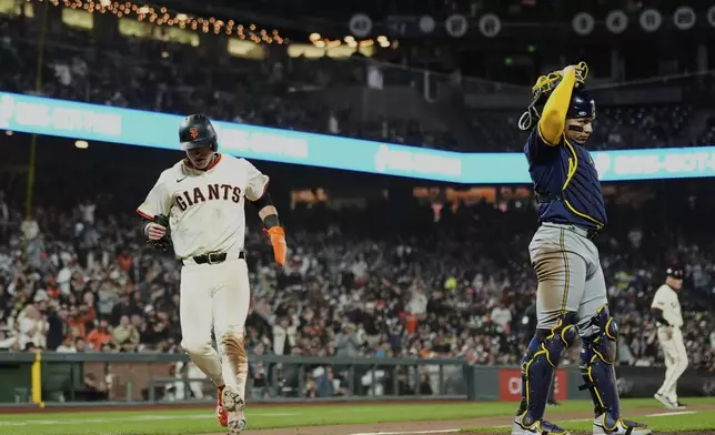 San Francisco Giants' Tyler Fitzgerald, left, scores next to Milwaukee Brewers catcher William Contreras on a throwing error by second baseman Brice Turang during the fifth inning of a baseball game Monday, April 21, 2025, in San Francisco. (AP Photo/Godofredo A. Vásquez)