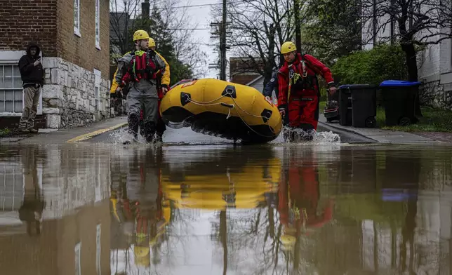 Search and rescue firefighters carry a boat to a flooded neighborhood on Sunday, April 6, 2025, in Frankfort, Ky. (AP Photo/Jon Cherry)