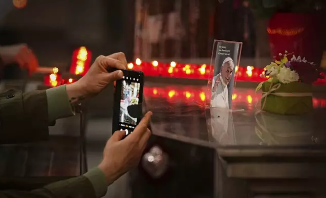 A woman takes a picture of a photograph of the late Pope Francis, that reads "Please, don't forget to pray for me" during a mass in his memory at the Chiesa di Santo Spirito in Sassia outside the Vatican, Thursday, April 24, 2025. (AP Photo/Andreea Alexandru)