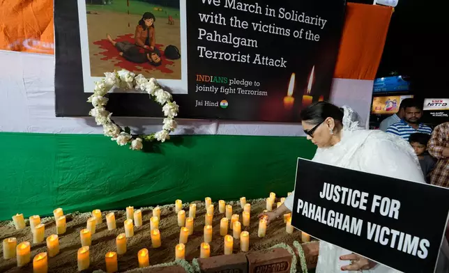 A woman puts a candle holding a banner during a protest and solidarity march against the killing of tourists by militants near Pahalgam in Indian controlled Kashmir, in Kolkata, India, Friday, April 25, 2025. (AP Photo/Bikas Das)