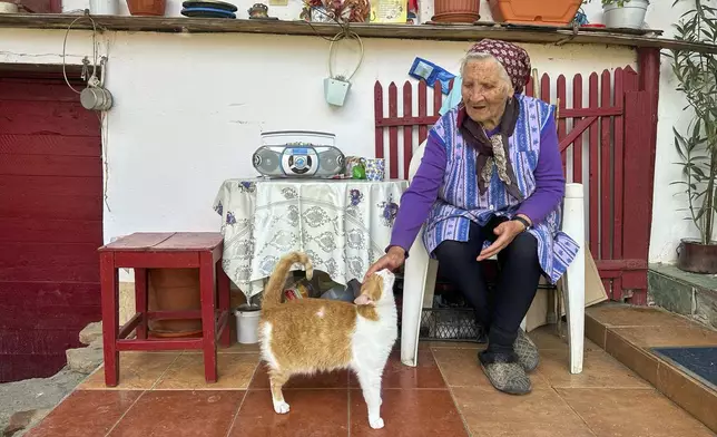 Zoica Roth, 83, pets her three-legged cat in the village of Saschiz, in Romania's central Transylvania region, Friday, April 25, 2025. (AP Photo/Stephen McGrath)