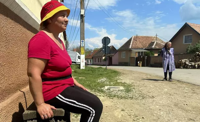 Monica Rosalea, 41, who periodically works abroad, sits on a wooden bench in the village of Saschiz, in Romania's central Transylvania region, Friday, April 25, 2025. (AP Photo/Stephen McGrath)