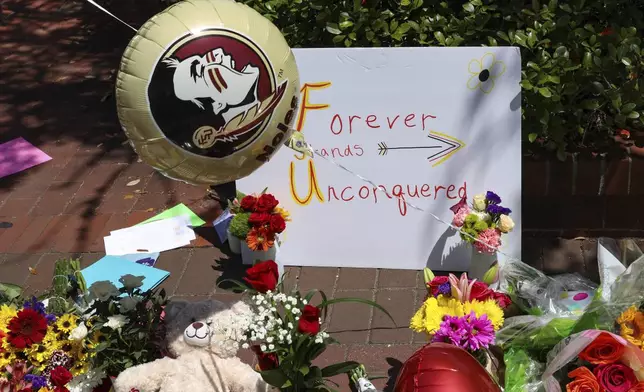 A sign that reads "Forever Stands Unconquered," is placed among flowers near the Florida State Student Union building, Tallahassee, Fla., Friday, April 18, 2025. (AP Photo/Gary McCullough)