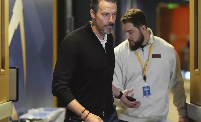 Denver Nuggets team president Josh Kroenke, left, hands off his mobile phone to the Nuggets' media relations manager Nick O'Hayre on the way in to respond at a news conference Monday, April 14, 2025, in Denver to questions about the firing of the team's general manager and head coach last week. (AP Photo/David Zalubowski)