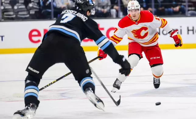 Calgary Flames center Yegor Sharangovich (17) and Utah Hockey Club defenseman Michael Kesselring (7) skate to gain possession of the loose puck during the second period of an NHL hockey game Tuesday, April 1, 2025, in Salt Lake City. (AP Photo/Tyler Tate)
