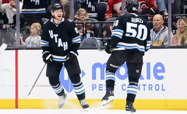 Utah Hockey Club center Barrett Hayton (27) and defenseman Sean Durzi (50) celebrate the goal scored by Hayton during the second period of an NHL hockey game against the Calgary Flames, Tuesday, April 1, 2025, in Salt Lake City. (AP Photo/Tyler Tate)