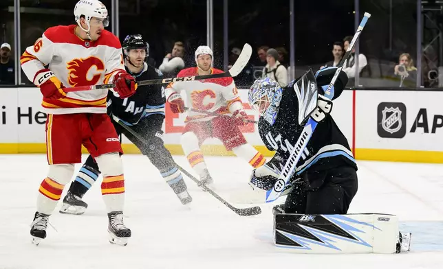 Utah Hockey Club goaltender Karel Vejmelka (70) defects the shot by Calgary Flames center Morgan Frost (16) up into the air during the second period of an NHL hockey game Tuesday, April 1, 2025, in Salt Lake City. (AP Photo/Tyler Tate)