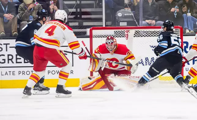 The puck is tipped in past Calgary Flames goaltender Dustin Wolf (32) by Utah Hockey Club center Barrett Hayton, left, during the second period of an NHL hockey game Tuesday, April 1, 2025, in Salt Lake City. (AP Photo/Tyler Tate)